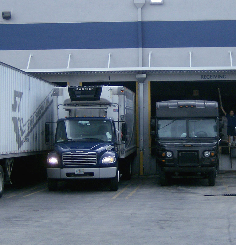 A few different sized trucks parked backwards to connect to a warehouse